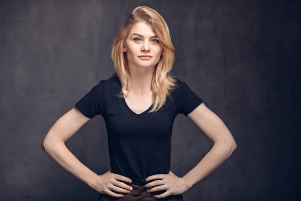 Portrait of beautiful female standing against black background. Young woman is wearing white dress. She is with hands in pockets.