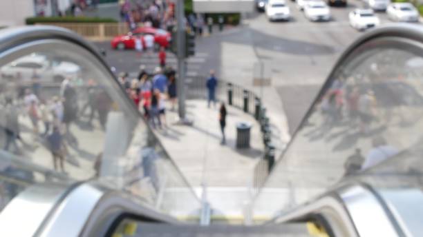 Perspective view thru escalator, defocused unrecognizable group of people on road intersection crosswalk on Strip of Las Vegas, USA. Anonymous blurred pedestrians on walkway in crowded urban downtown