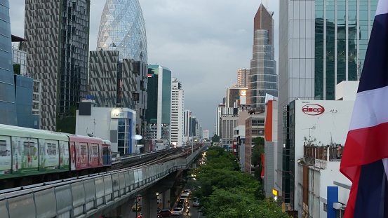 Bangkok, Thailand - 10 July, 2019: View of modern asian city from bts sky train platform. Train on metro rail road station. Public transportation in Krungtep downtown. State national flag waving