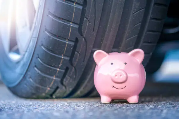 Photo of Pink piggy bank sits next to the new tire of a modern car