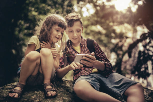 istock Two kids using smart phone sitting on a big rock in the forest 1259959518