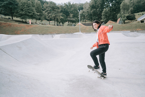 a young chinese girl practising skateboarding in the public skateboarding park during weekend