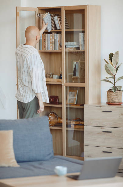 istock Bald Woman Putting Book in Bookcase at Home 1260017577