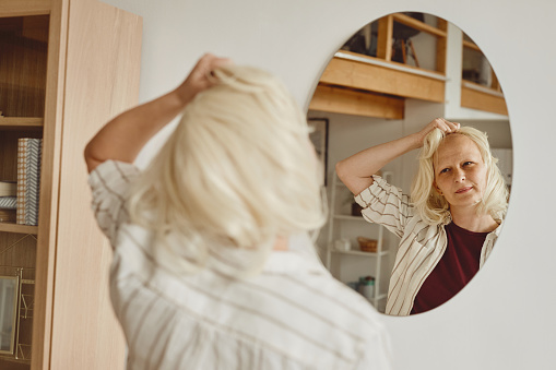 Mujer calva moderna tomando wig por espejo photo