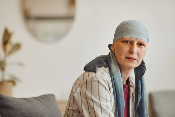 Mature Woman Wearing Headscarf Warm-toned portrait of bald adult woman wearing headscarf looking at camera while posing in minimal home interior, alopecia and cancer awareness, copy space cancer illness stock pictures, royalty-free photos & images