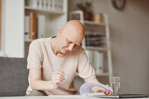 Warm toned portrait of adult bald woman filling in patients form at doctors office during alopecia and cancer recovery, copy space