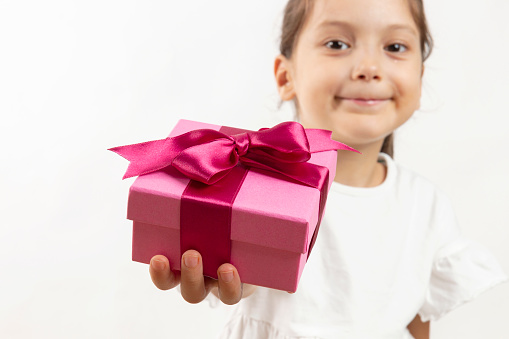 Little child girl holding pink gift box with white silky ribbon on white background. Happy birthday party concept