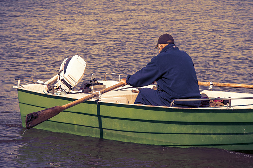 Senior men boating with paddle rear view. Old man rowing a rowboat with oars back viewed. Senior men recreation in summertime. Lonely pensioner and his hobby. Active old person photography.