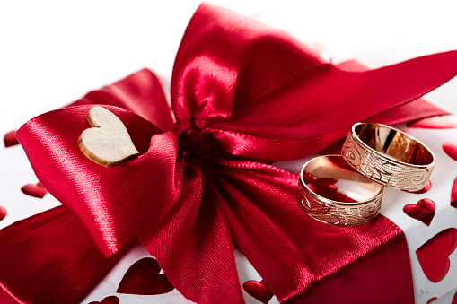 Gift wrapping, a box with a surprise for the holiday, wrapped in white paper with red hearts, and tied with a red ribbon in the shape of a bow. Holiday gift, love concept.