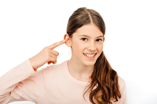 Pretty girl point on her ear and smiling. My hearing is perfect. Child hearing exam and hearing treatment concept