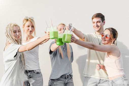 Group of young people toasting with green organic smoothie drinks