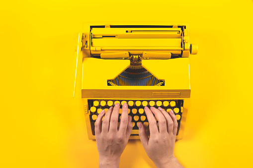 Female hands on yellow bright typewriter on a yellow. Symbol for writing, blogging, new ideas and creativity