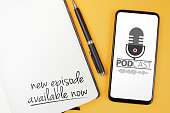 podcasting concept, text NEW EPISODE AVAILABLE NOW written on note pad and smartphone with podcast player mockup