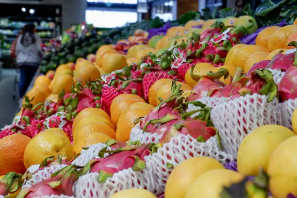 Fruit shop greengrocer display shelf with exotic fruits - mangooes, dragonfruits, oranges, avocadoes