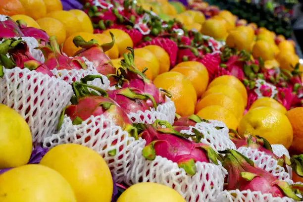 Fruit shop greengrocer display shelf with exotic fruits - mangooes, dragonfruits, oranges, avocadoes