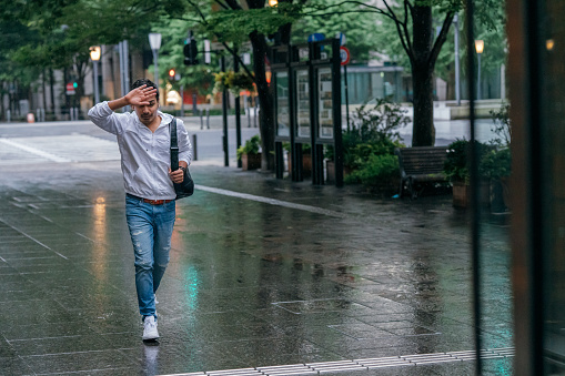 A young man is unprepared for the rain and trying to escape from the rain without an umbrella in the city.