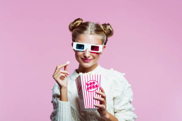 Portrait of happy teenege girl watching 3d movie Portrait of teenager wearing white sweater and 3d glasses. Girl holding popcorn, smiling at camera. Studio shot on pink background. 3 d glasses stock pictures, royalty-free photos & images