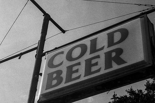 Old fashioned beer sign board outside liqour store. Shot on a 35mm roll of Ilford HP5 Plus