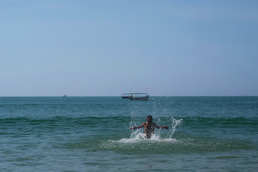 Stock photo showing laughing Indian man wearing swimming goggles whilst waist deep in water of the Indian Ocean, Palolem beach, Goa, India.