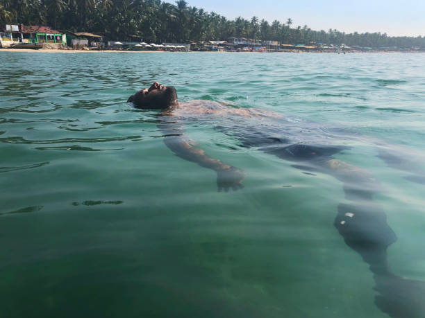 image of indian man on beach holiday vacation, swimming and splashing in indian ocean, surface level of glistening, choppy water surface wave, palolem beach, goa, india - goa beach india green imagens e fotografias de stock