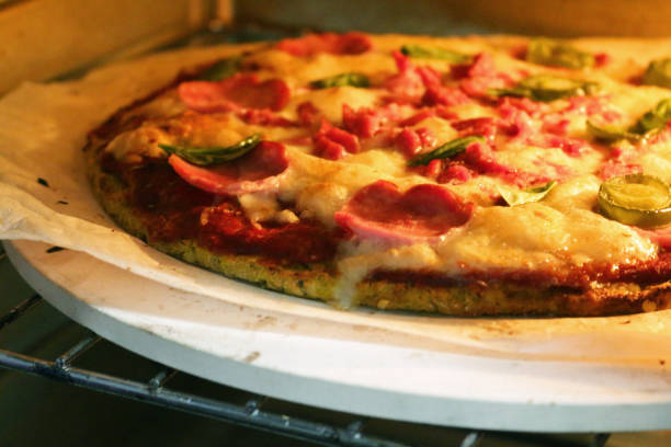 istock Image of cooked homemade cauliflower base pizza baking in oven, cooked on pizza stone for thin and crispy base, pepperoni and fresh basil leaves on top 1260332518