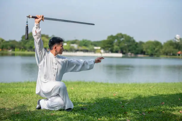 Photo of Asian man doing Tai Chi sword in the park.
