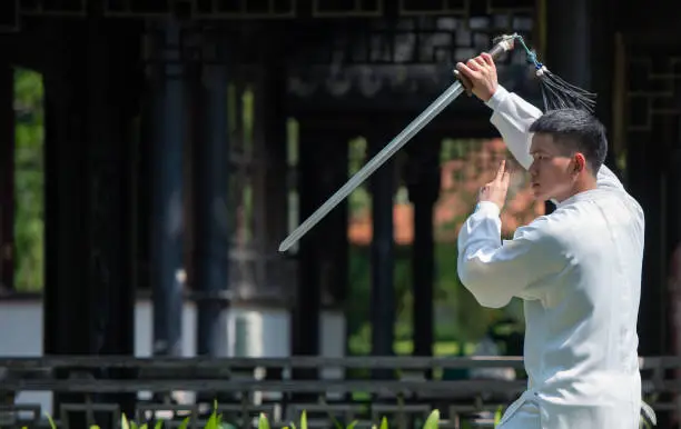 Photo of Asian man doing Tai Chi sword in the park.