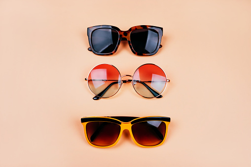This is a close up photograph of a pair of sunglasses. One is for men the other is for women sitting on top of a green striped beach towel on a wood deck. There is space for a copy