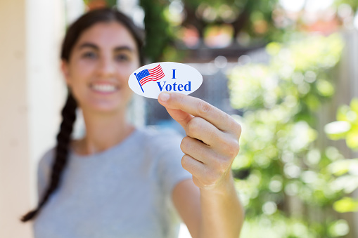 Young woman holding I voted sticker with American flag.