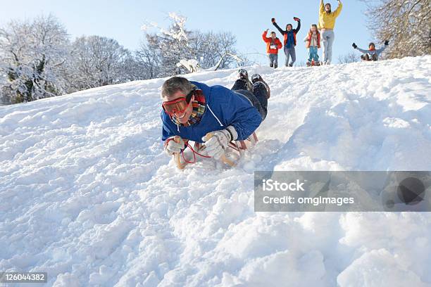 Homem Sledging Colina Com A Família A Olhar Para Baixo - Fotografias de stock e mais imagens de Trenó - Equipamento de Recreio