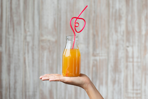 Caucasian female is holding a bottle of fruit juice with heart shaped straw.