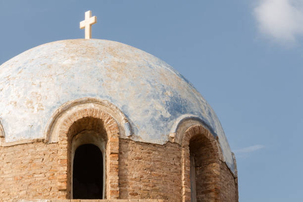 Blue weathered dome with white cross against blue sky.