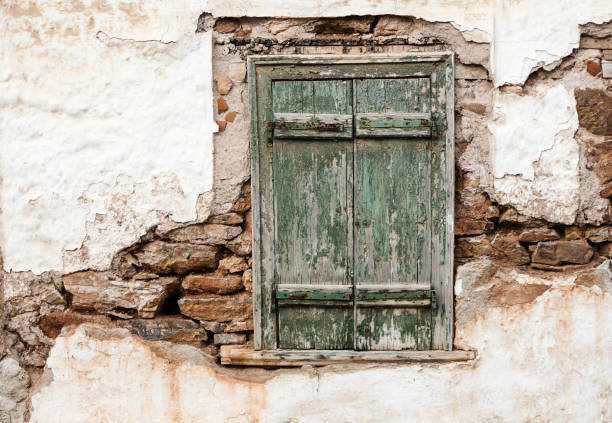 Old wooden window with green shutters on weathered wall.