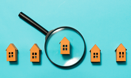 Blue background with paper houses and magnifier.  Concept of rent, search, purchase real estate.