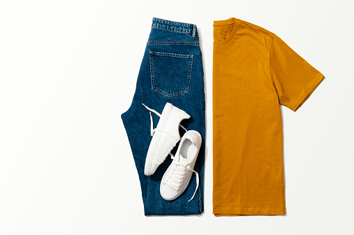Orange t-shirt, blue jeans and white sneakers on white background