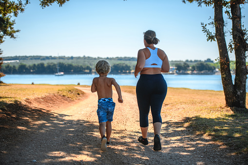 Caucasian mother and son running on the seaside on a sunny day in Croatia. Sea is front of them.