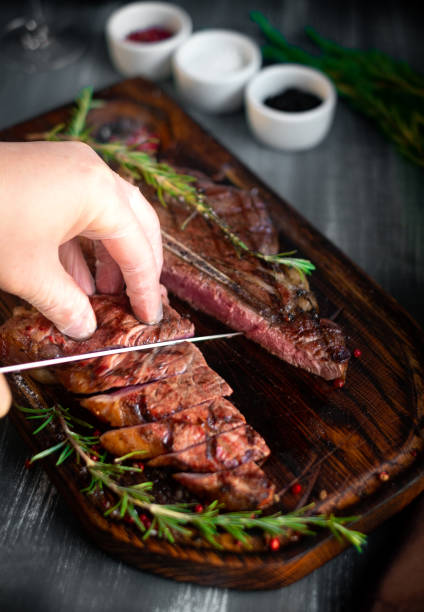 istock Man hand cutting grilled t bone steak on wooden board 1260550939