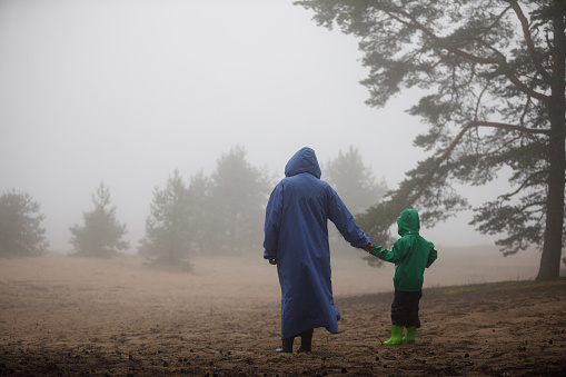 Mother and son walk along the foggy shore. A woman with a boy in raincoats in nature.