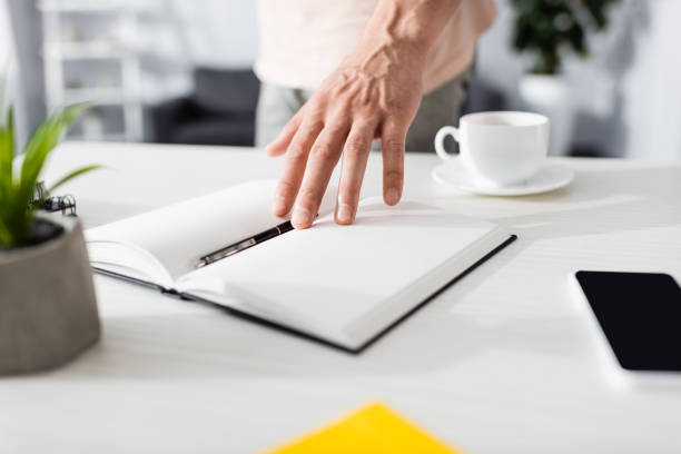 Cropped view of man pointing with hand at notebook at home