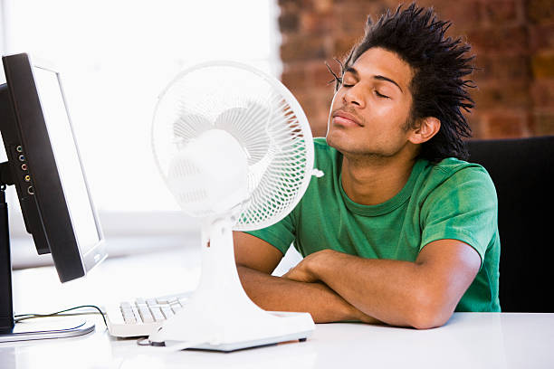 jovem no escritório com soprando ventilador elétrico - office fan - fotografias e filmes do acervo