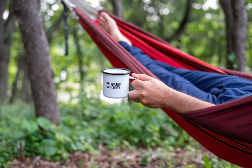 Man relaxing in a hammock with a coffee mug that says Probably Whiskey
