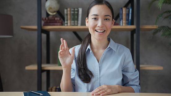 Smiling young asian woman teacher conducts online lesson looking at camera