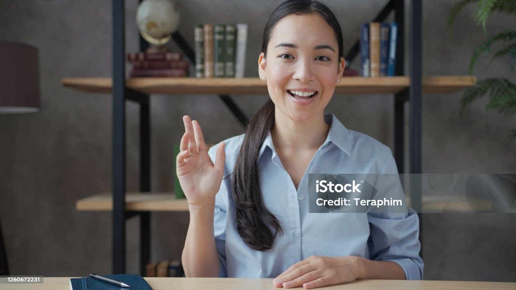 Smiling young asian woman teacher conducts online lesson looking at camera Talking Stock Photo