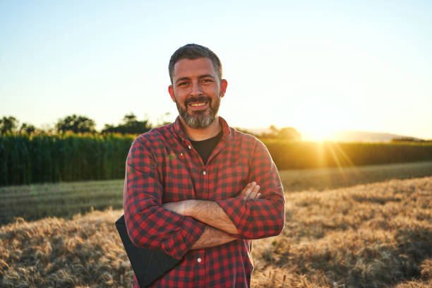Portrait of a proud and satisfied man standing in a wheat field Modern mid adult man with a digital tablet working and examining the quality of a wheat field in summer. man beard plaid shirt stock pictures, royalty-free photos & images