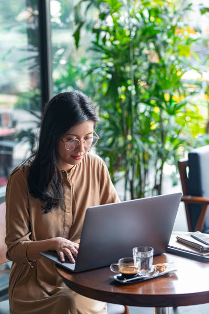 Asian Woman/ College Student Using a Laptop Computer to Study Remotely at a Cafe