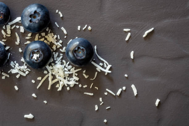 Fresh blueberries and shredded coconut on dark slate, top view.