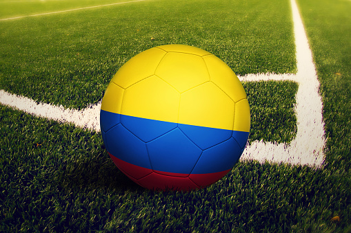 Colombia flag on ball at corner kick position, soccer field background. National football theme on green grass.
