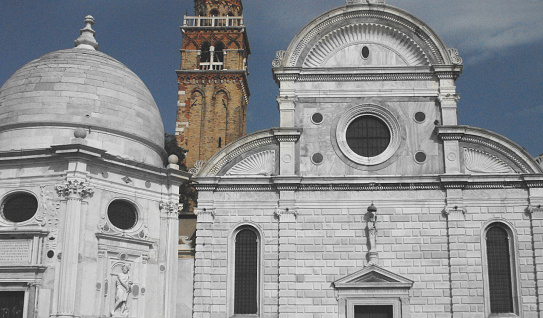 Architectural details in a close up of an ancient, historic cathedral with arches, a dome, round windows, with a red brick bell tower in the background.  Shot from a ferry in Venice, Italy.
