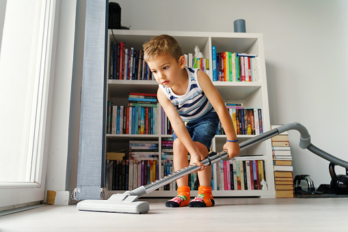 Little kid using vacuum cleaner at home - Small boy cleaning floor in apartment - Child doing housework having fun - side view full length in summer day - childhood development real people concept