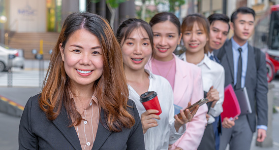 A group of Asian corporate workers stand in line facing camera smiling happy